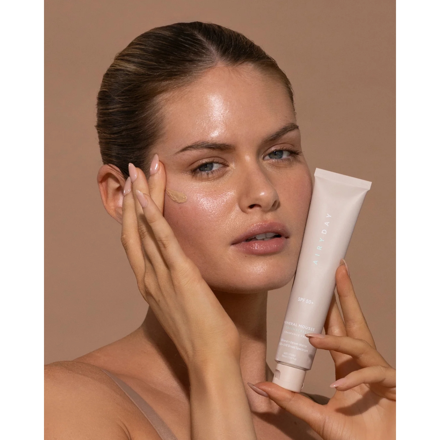 A model holding a tube of Airyday Mineral Mousse Skinscreen while touching her face against a beige background, featured in the brand's UK launch announcement on Beauty News Daily.