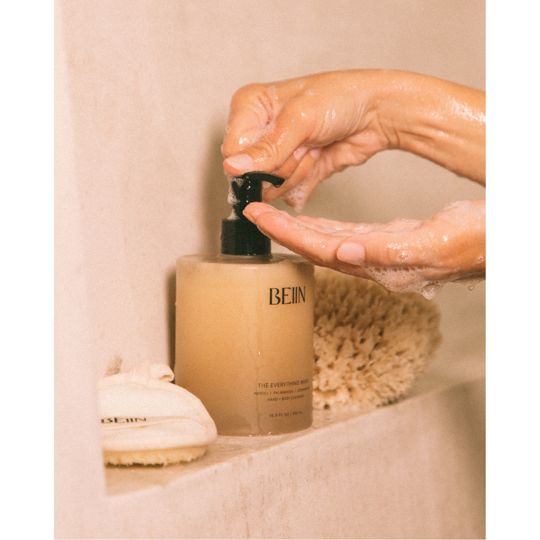 Soapy hands pump Beiin The Everything Wash on a shower ledge, with a sea sponge and a Beiin-branded cloth beside it