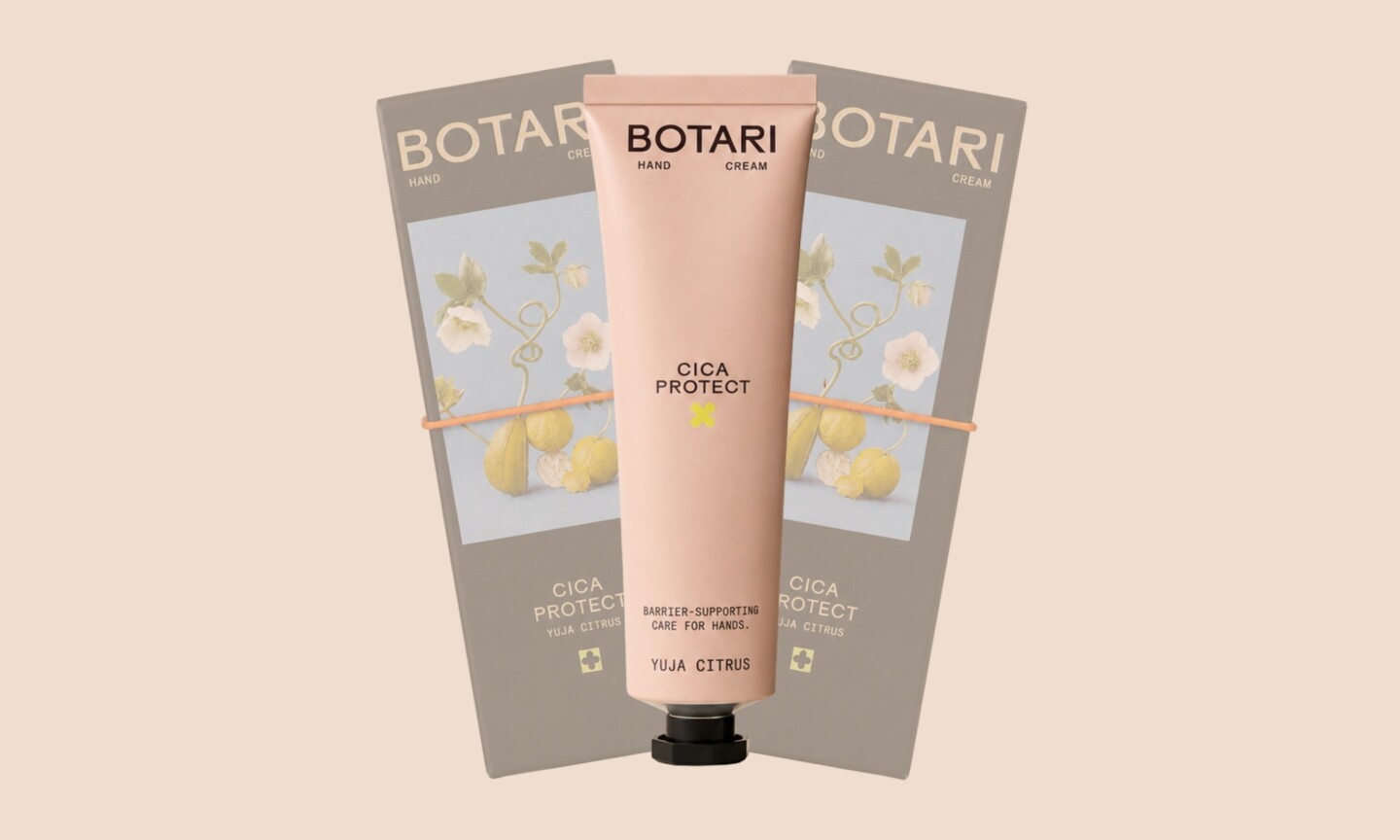 A blush pink tube of Botari Cica Protect Yuja Citrus hand cream centered in front of two gray packaging boxes arranged in a fan display on a light beige background.