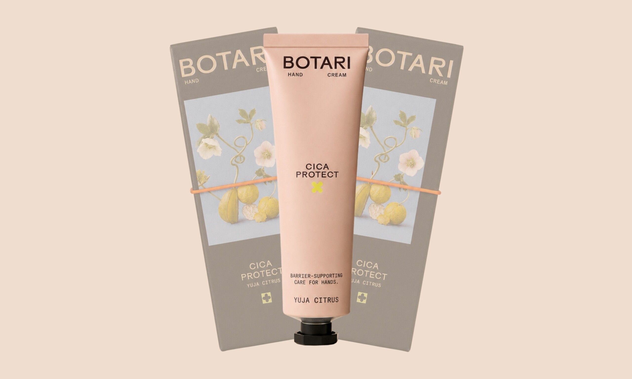 A blush pink tube of Botari Cica Protect Yuja Citrus hand cream centered in front of two gray packaging boxes arranged in a fan display on a light beige background.