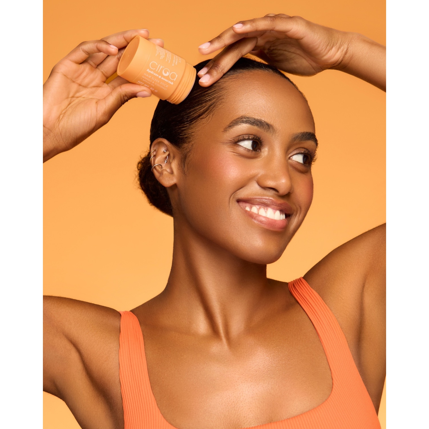 Smiling model applying the Ciroa Mango and Coconut Hair Sleek Stick to smooth her hair back, featured on Beauty News Daily.