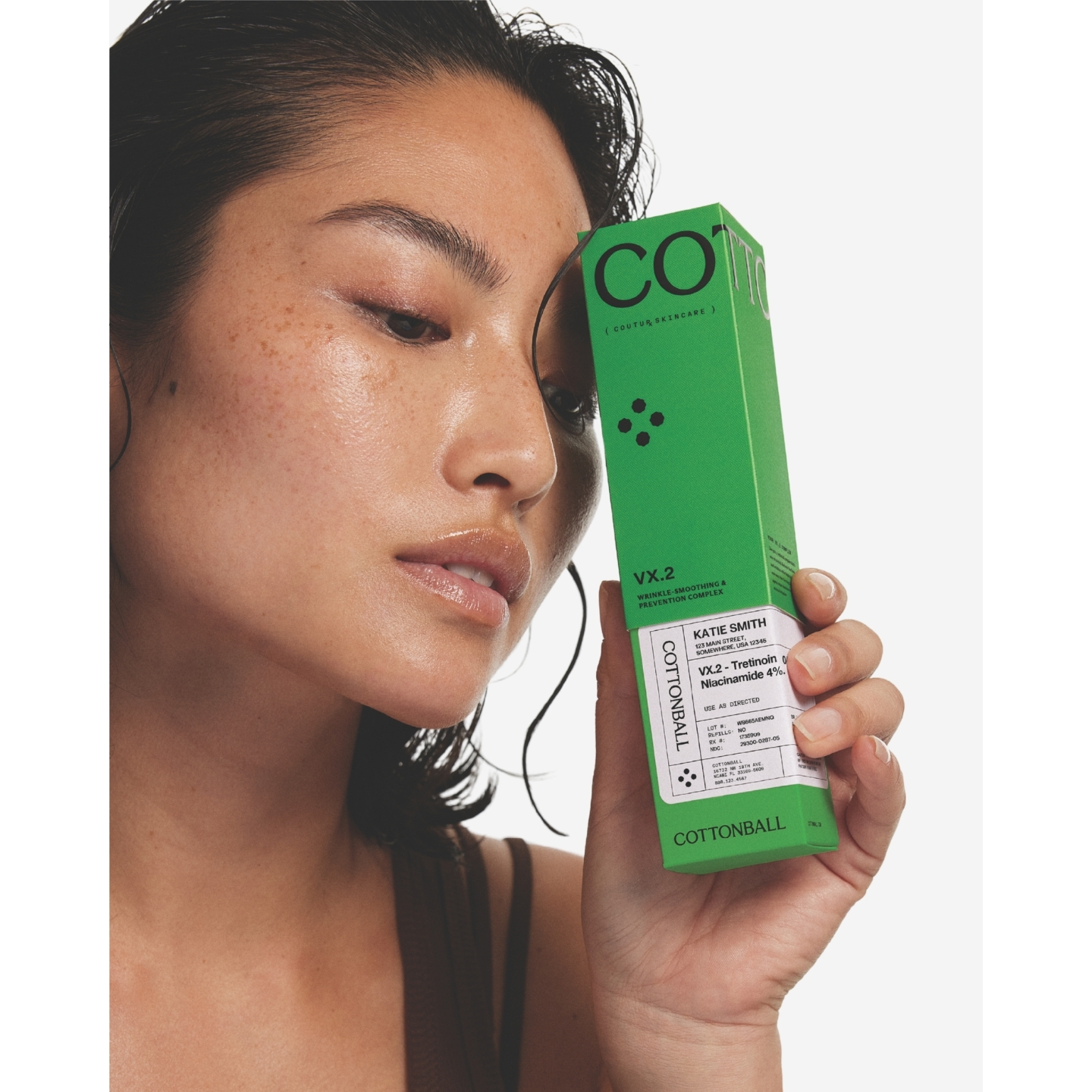 Close-up of a model resting her forehead against a bright green box of Cottonball VX.2 Wrinkle-Smoothing & Prevention Complex featuring a prescription label.