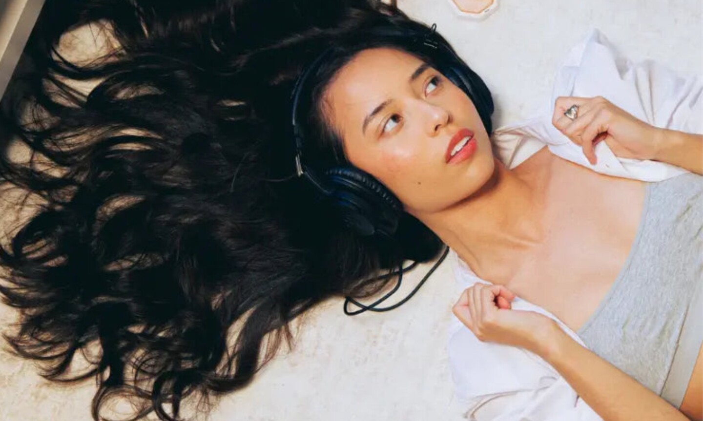 A model with long, wavy dark hair lying down while wearing over-ear headphones, featured in the Decibel haircare UK launch announcement on Beauty News Daily.