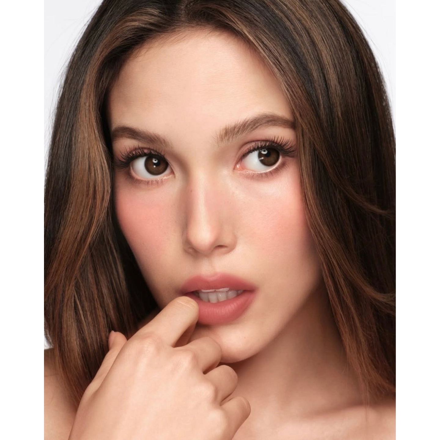 Extreme close-up portrait of Olympic champion skier Eileen Gu as global makeup ambassador for Armani Beauty, displaying luminous skin, flushed cheeks, and nude-pink lips with her finger gently resting against her mouth.
