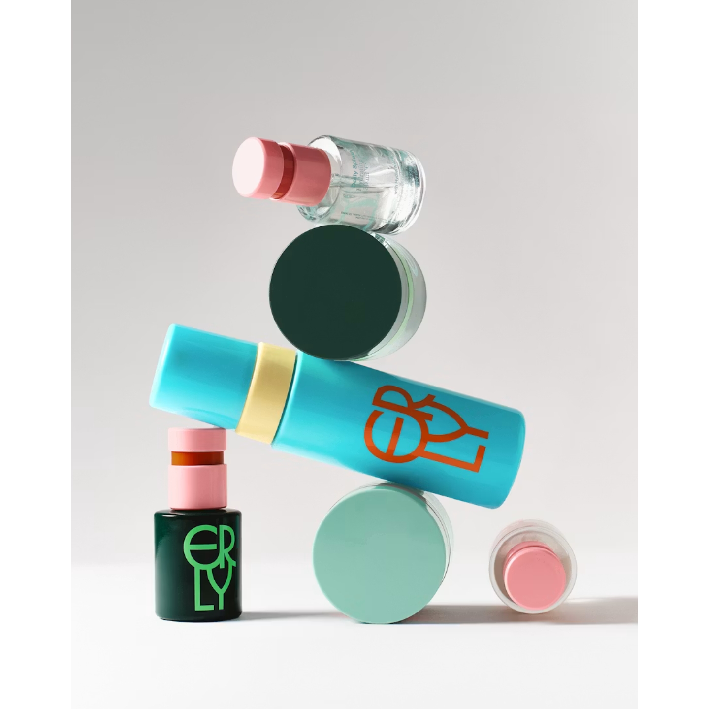 An artistic, vertically balanced stack of colorful ERLY skincare bottles and jars in vibrant shades of blue, green, and pink, featured in an interview with co-founder Dr. Hallie McDonald on Beauty News Daily.