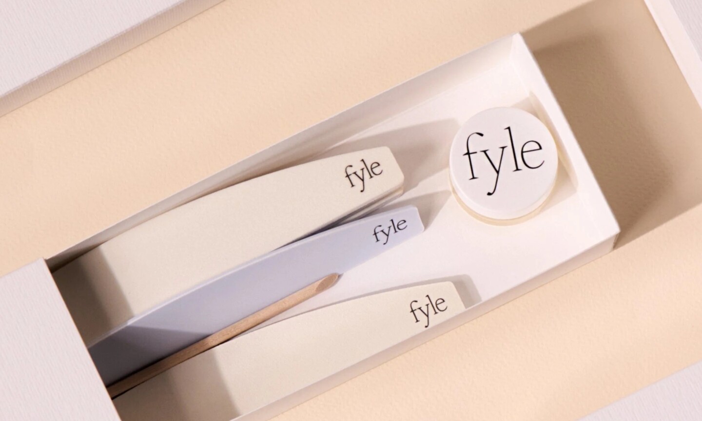 An open white box displaying the Fyle nail care kit with branded nail files, a cuticle stick, and a small round tub on a neutral background.