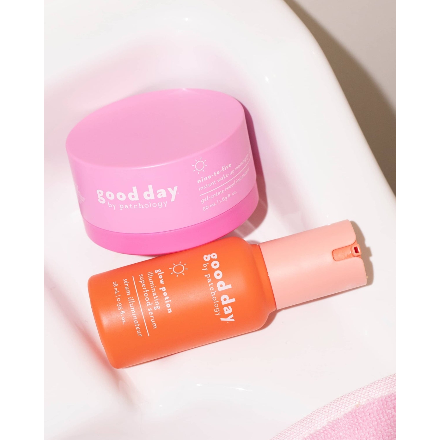 Good Day by Patchology Nine-to-Five Instant Wake-Up Morning Gel cream tub in bright pink resting next to an orange bottle of Glow Potion Illuminating Superfood Serum on a smooth white surface.
