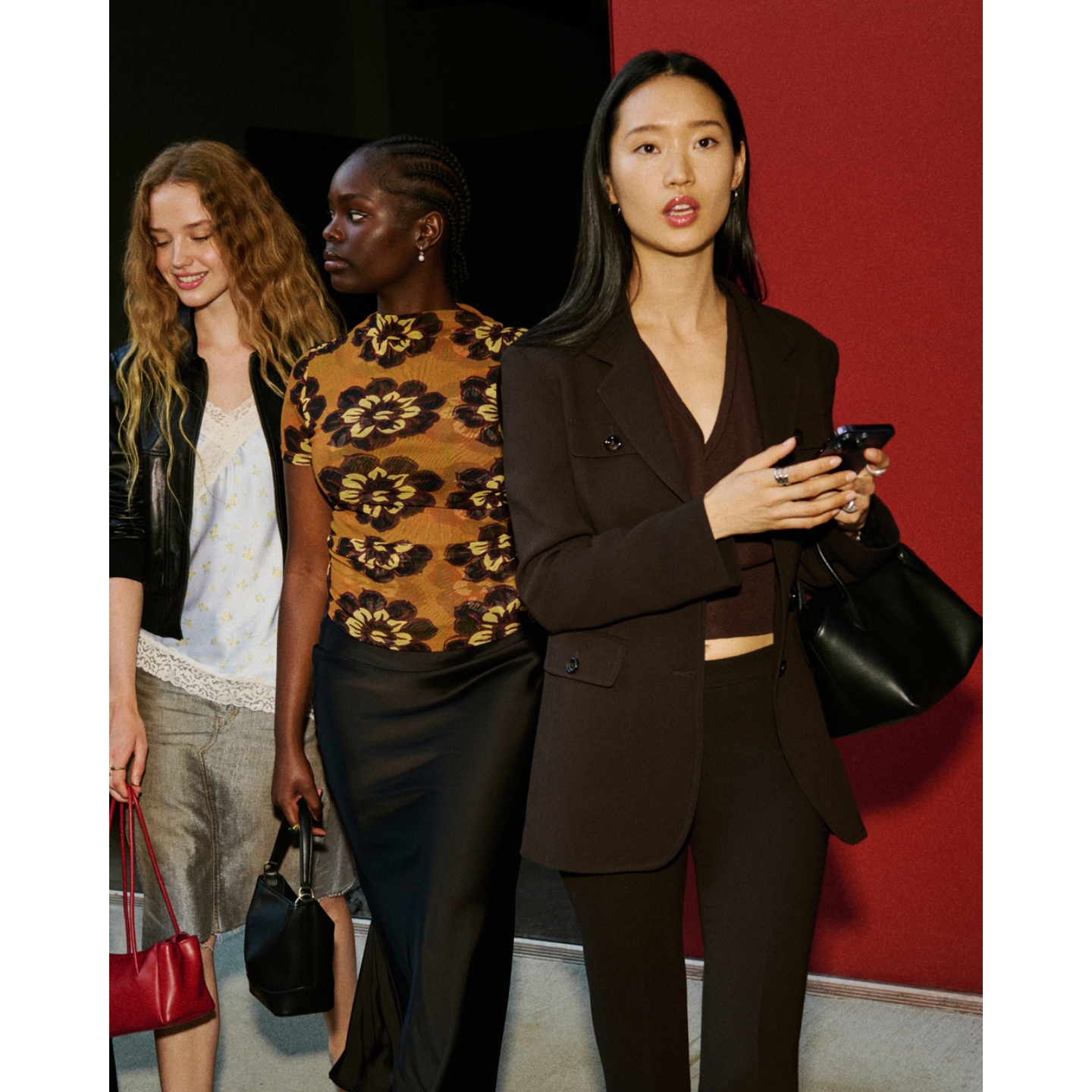 Three models walking together in tailored fashion looks, with one carrying a phone and black handbag in a campaign shoot for Gregg Renfrew's Beecee brand.