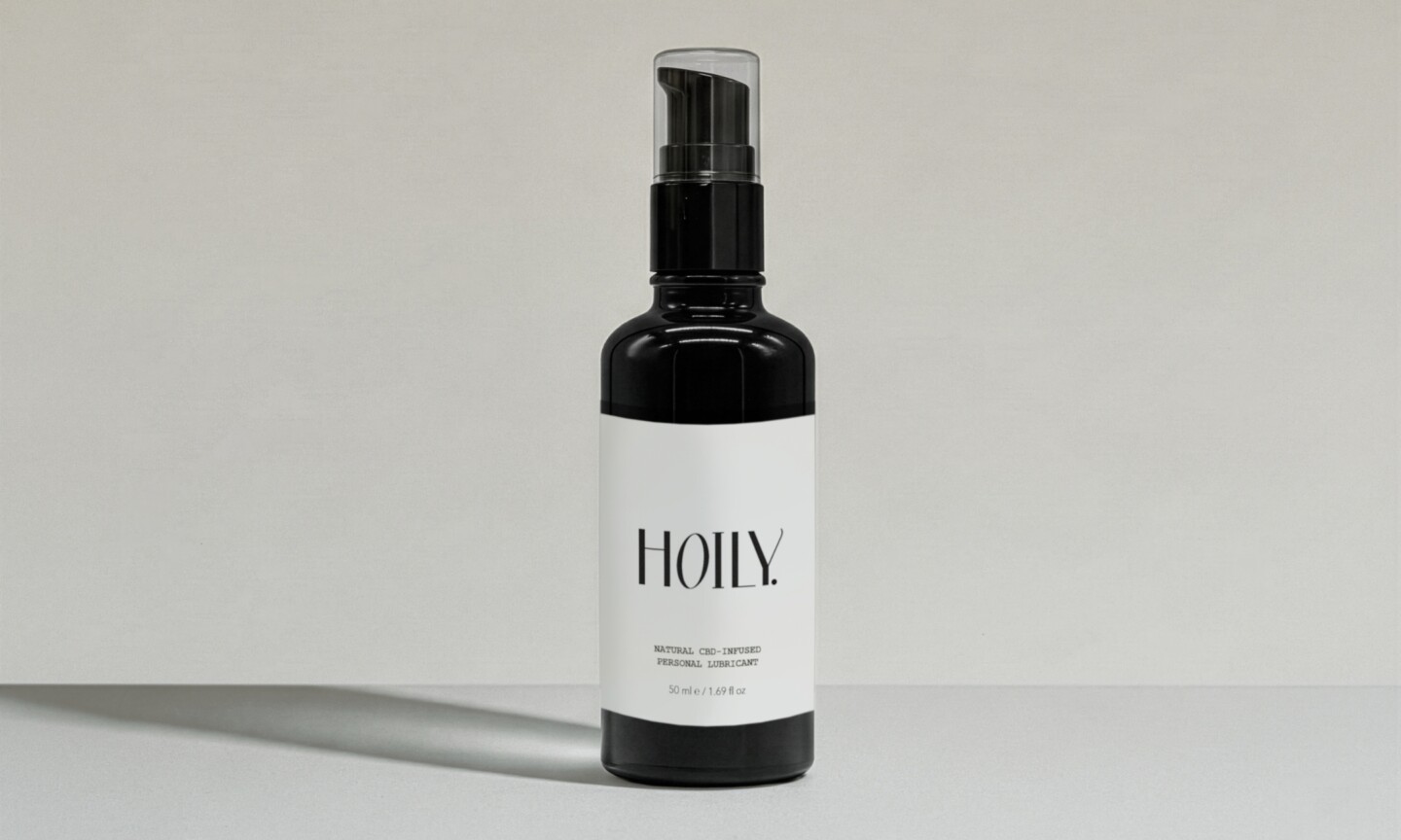 A dark amber glass pump bottle of Hoily Natural CBD-Infused Personal Lubricant with a minimalist white label on a light gray background.