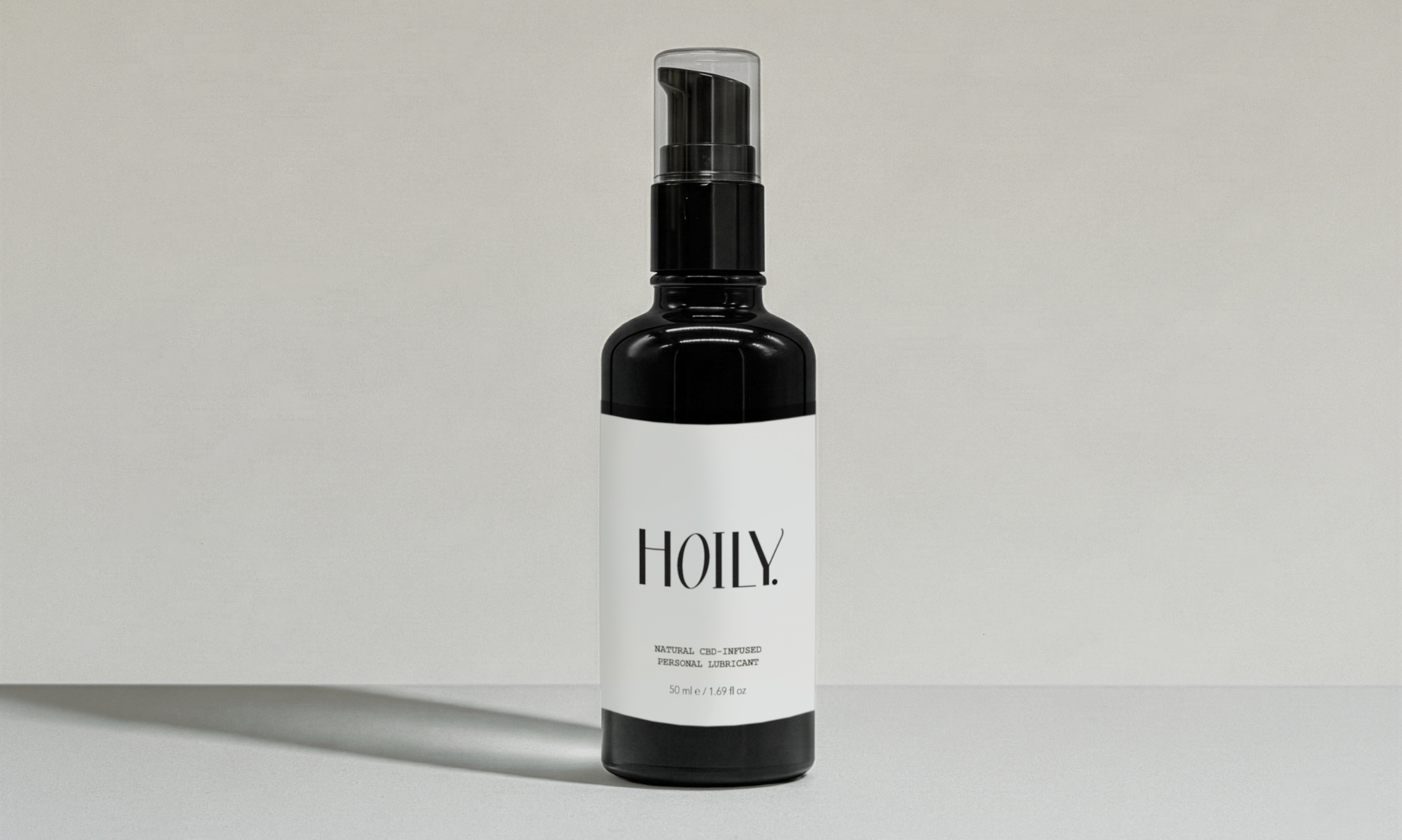 A dark amber glass pump bottle of Hoily Natural CBD-Infused Personal Lubricant with a minimalist white label on a light gray background.