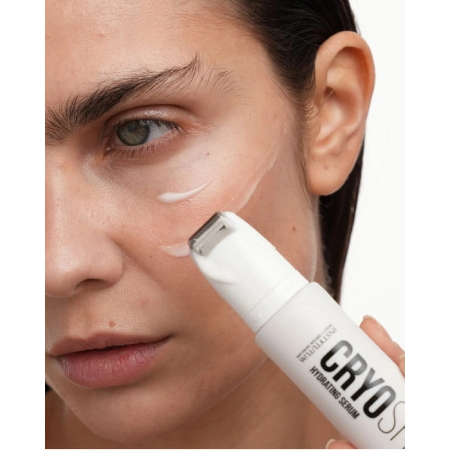 Close-up of a model using the metal applicator tip of an Instytutum CryoShot Hydrating Serum tube to glide product across her cheek.