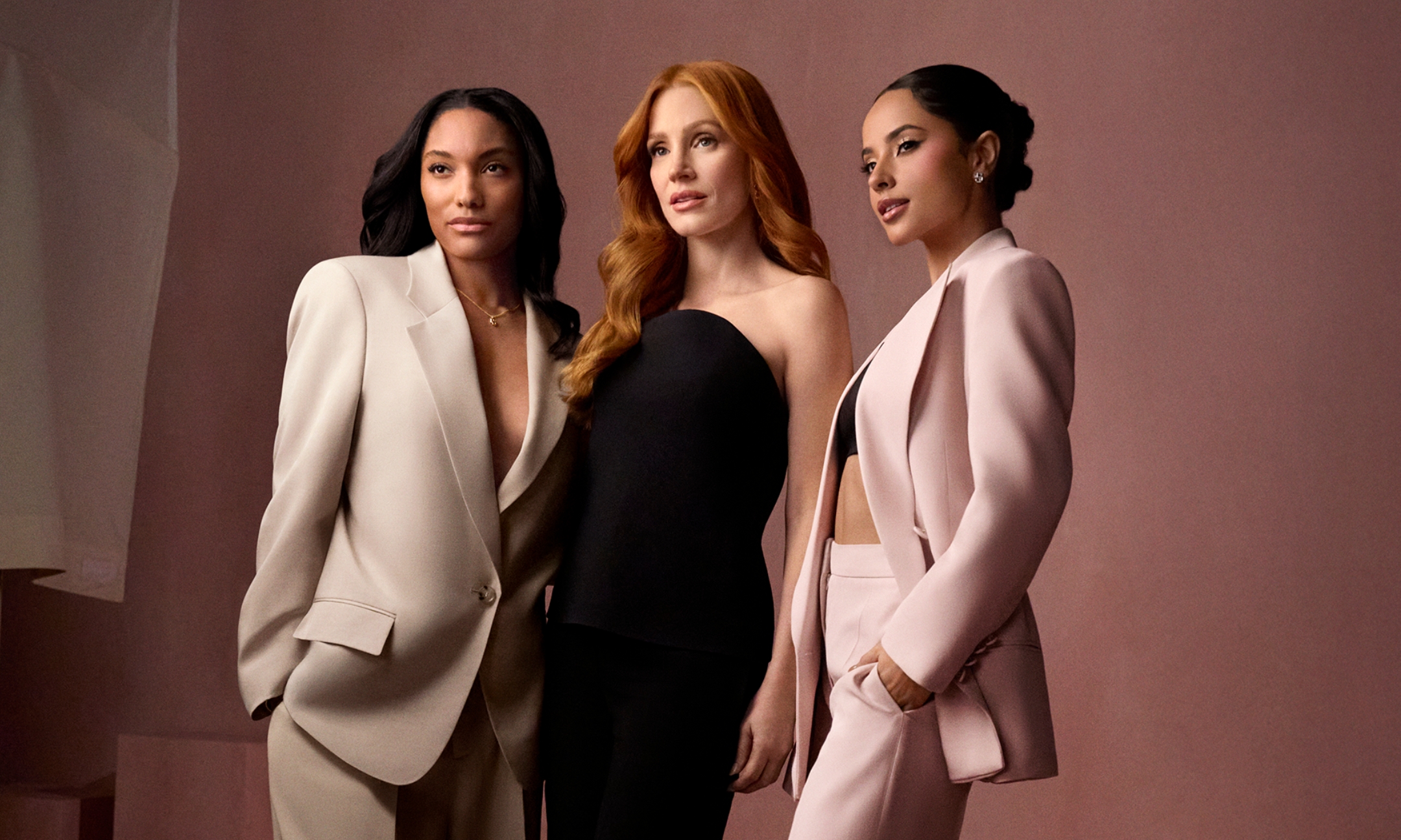 Tara Davis-Woodhall, Jessica Chastain, and Becky G posing together in tailored suits and formal wear for the Boss Bottled Beyond for Her campaign, featured on Beauty News Daily.