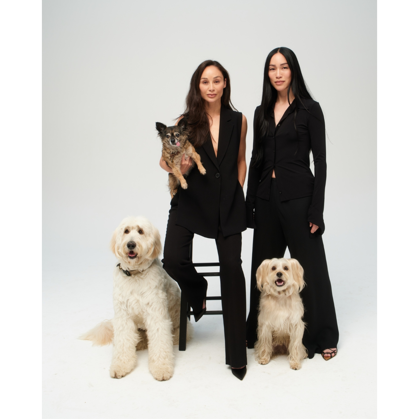 Lil Luv Dog co-founders Cara Santana and Stephanie Suganami wearing all-black outfits posing with three dogs against a plain white studio background.