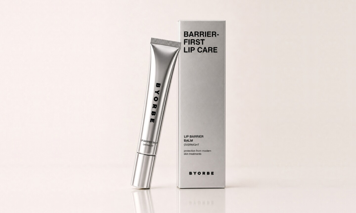 A metallic silver tube of Byorbe Lip Barrier Balm Overnight leaning against its matching silver outer box on a light neutral background.