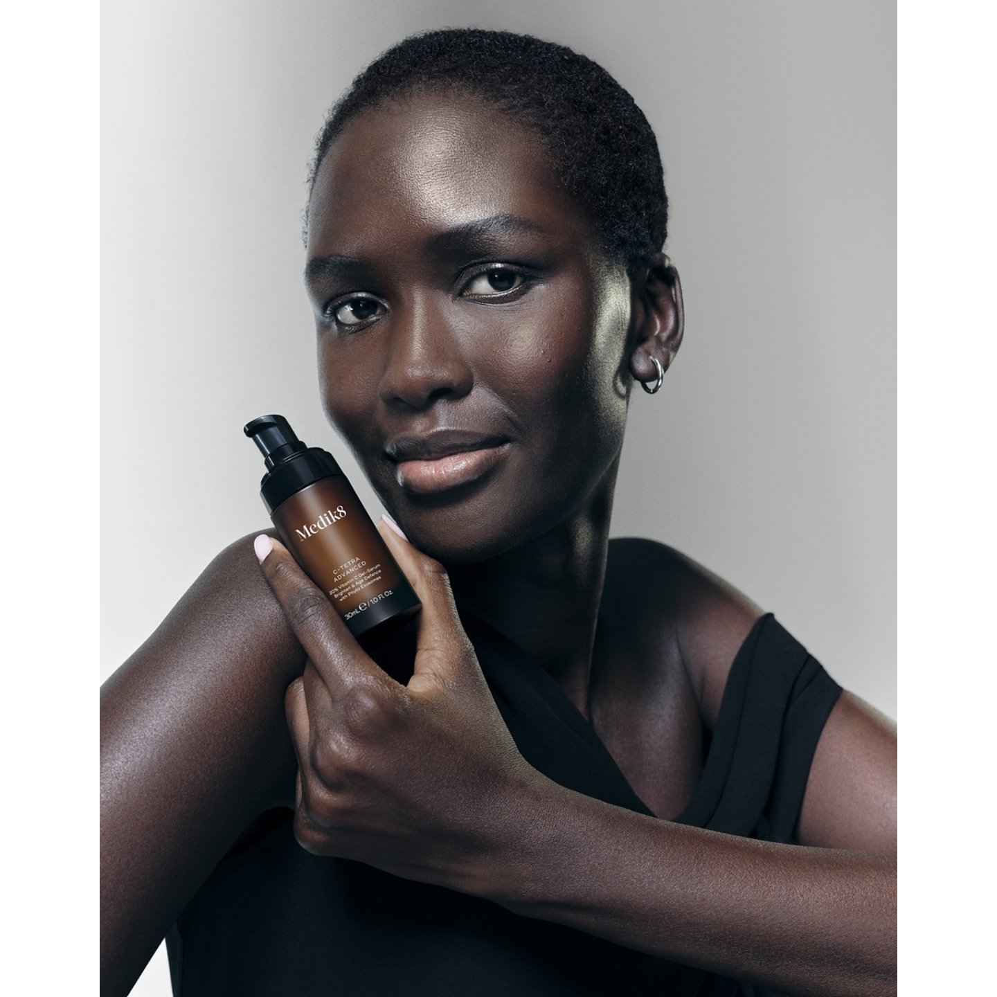 A model with a close-cropped haircut holding an amber bottle of Medik8 C-Tetra Advanced Serum against her shoulder, featured in the brand's Sephora US launch announcement on Beauty News Daily.