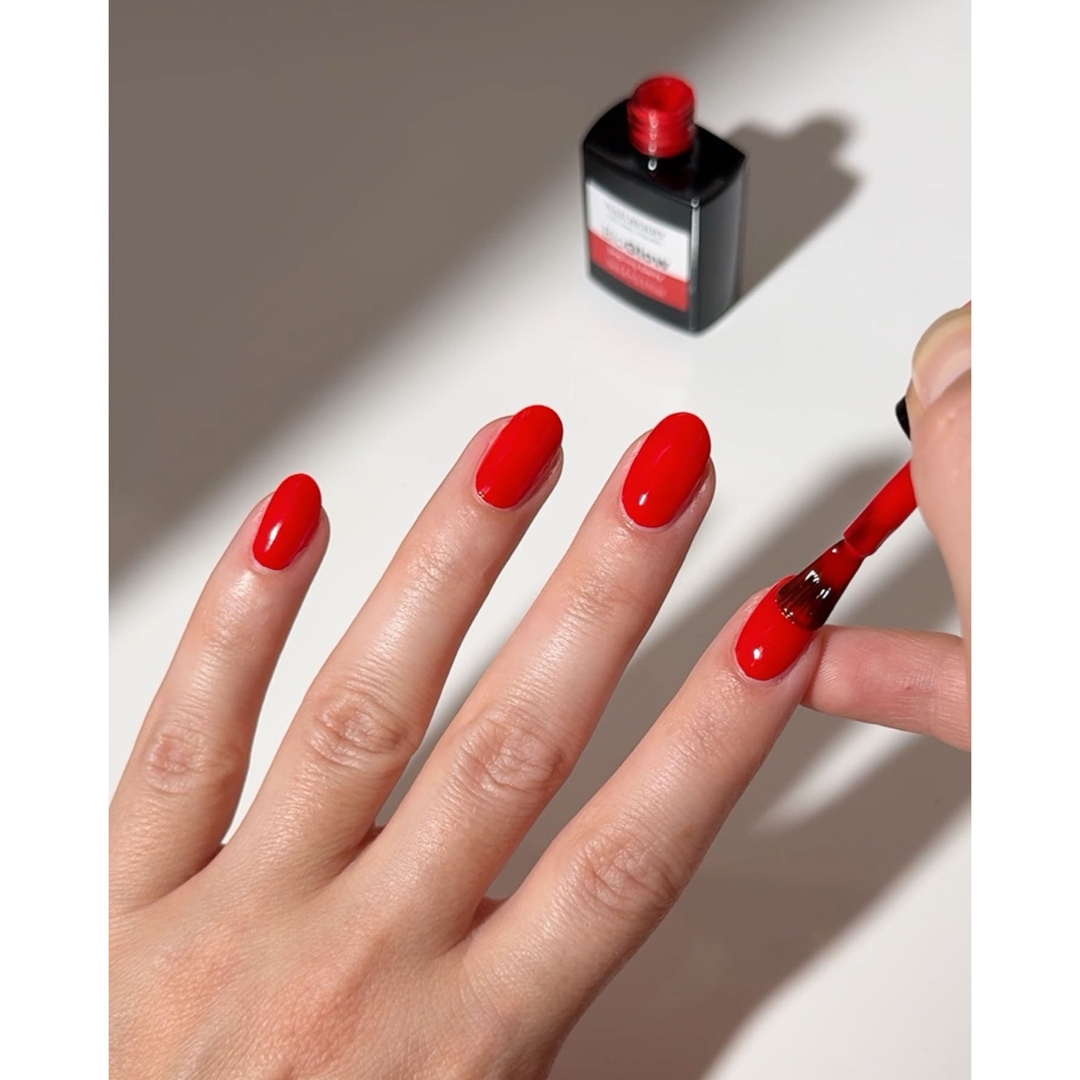A hand receiving an application of bright red Nailberry BioGlow LED Nail Polish with an open bottle in the background.