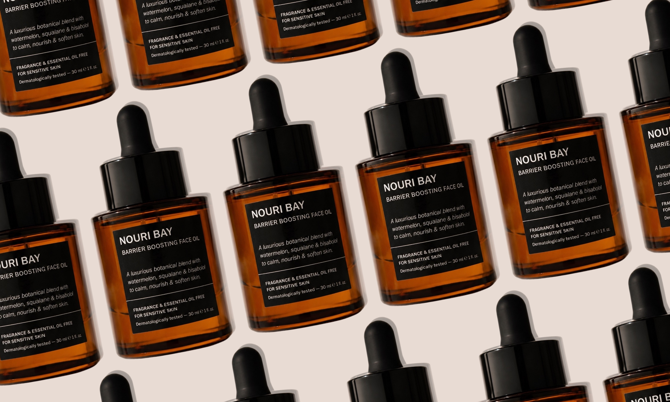 A repeating diagonal grid pattern of amber glass Nouri Bay Barrier Boosting Face Oil dropper bottles set against a beige background.