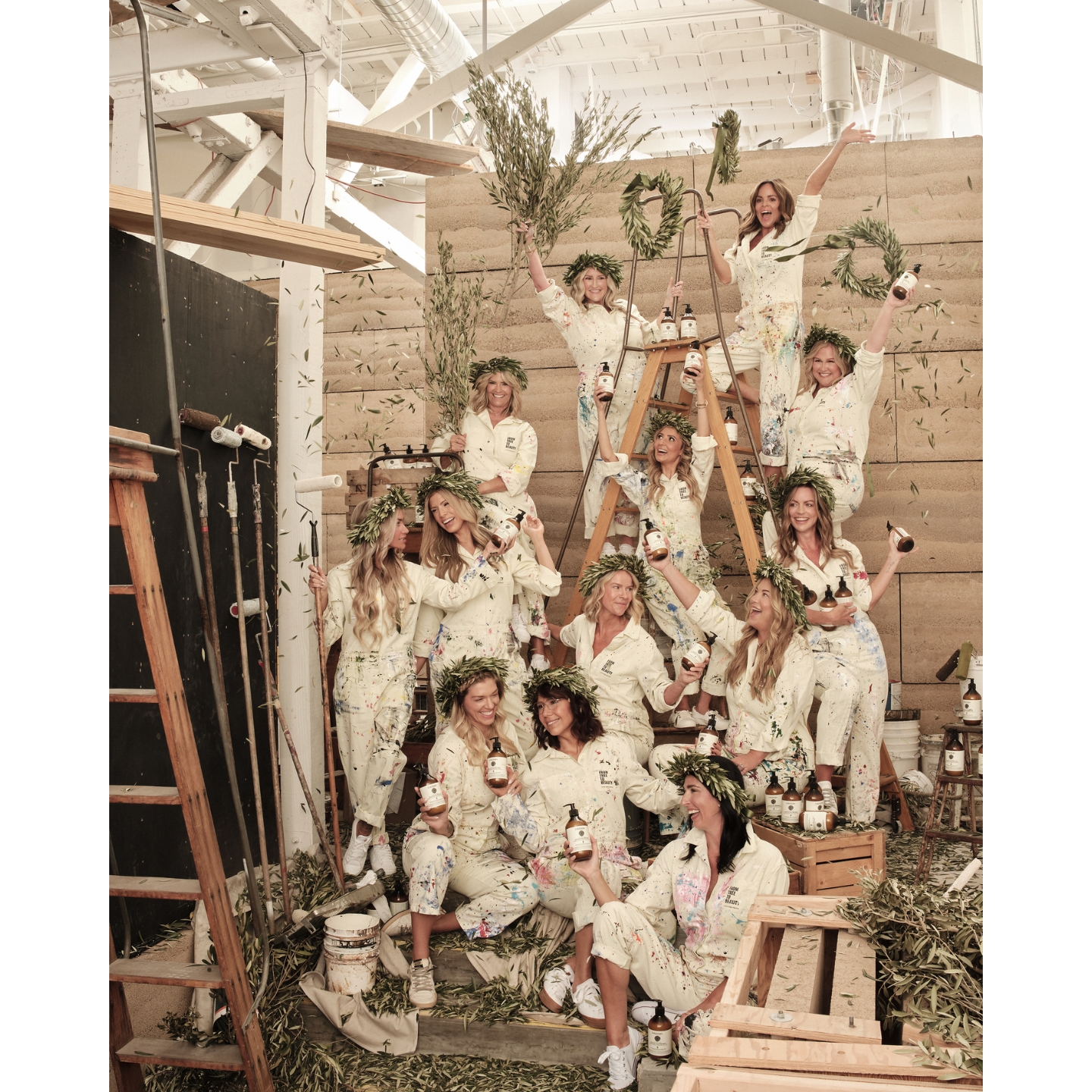 A group of women in paint-splattered white jumpsuits and olive branch crowns holding Olive Tree People products inside the brand's Abbot Kinney flagship store in Venice, California.