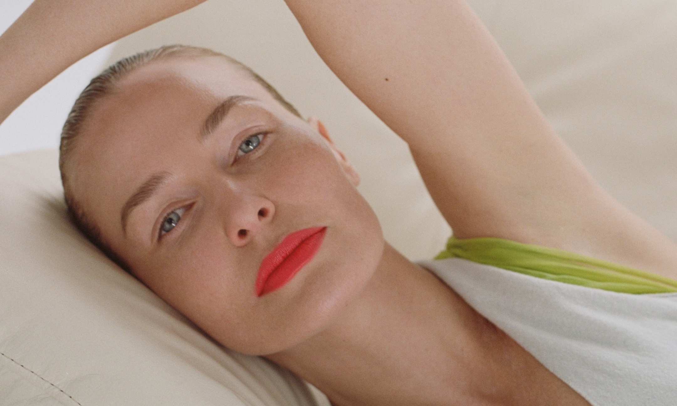 Lara Worthington lying down with slicked-back hair and bright red lipstick, extending one arm above her head.