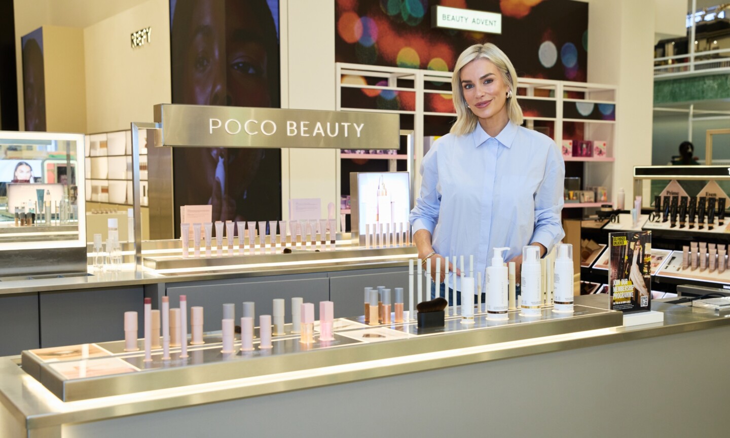 Pippa O'Connor standing behind a illuminated metal Poco Beauty display counter filled with makeup products inside Selfridges.