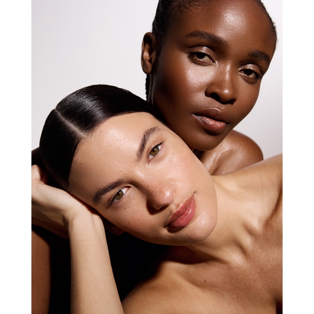 Close-up beauty portrait of two models with slicked-back hair showcasing natural, glowing skin.