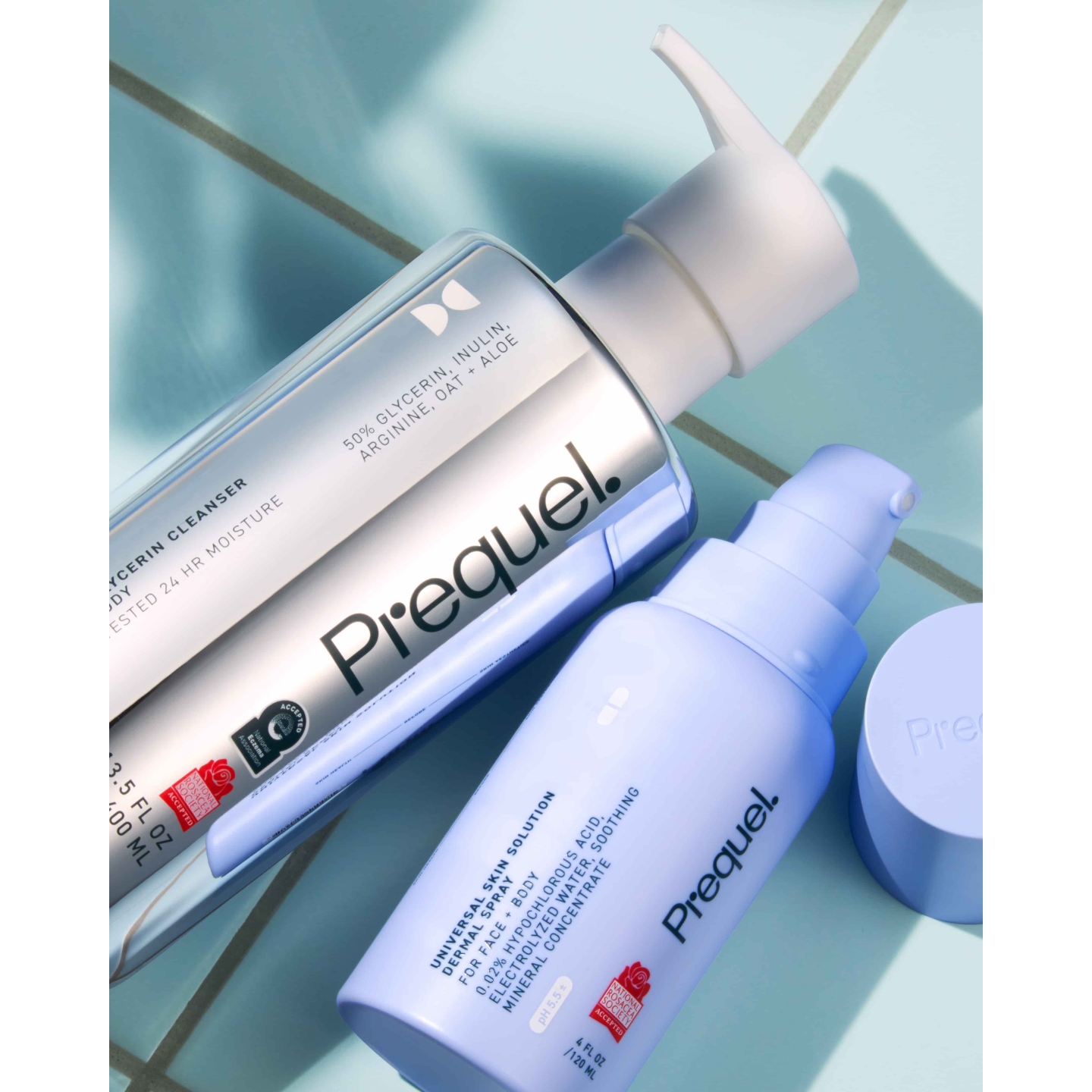 A bottle of Prequel Universal Skin Solution Hypochlorous Acid Dermal Spray resting next to a chrome pump bottle of Prequel Gleanser Glycerin Cleanser on a light blue tiled surface.