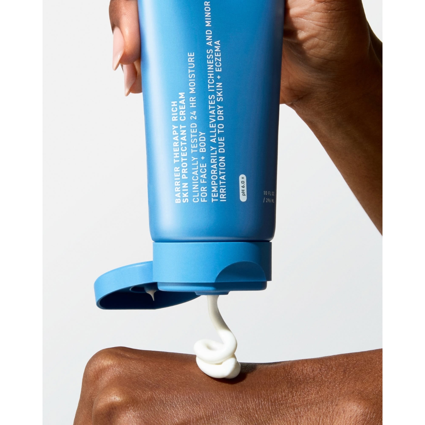 A hand holding a blue squeeze tube of Prequel Barrier Therapy Rich Skin Protectant Cream upside down, dispensing a dollop of white cream onto the back of another hand.