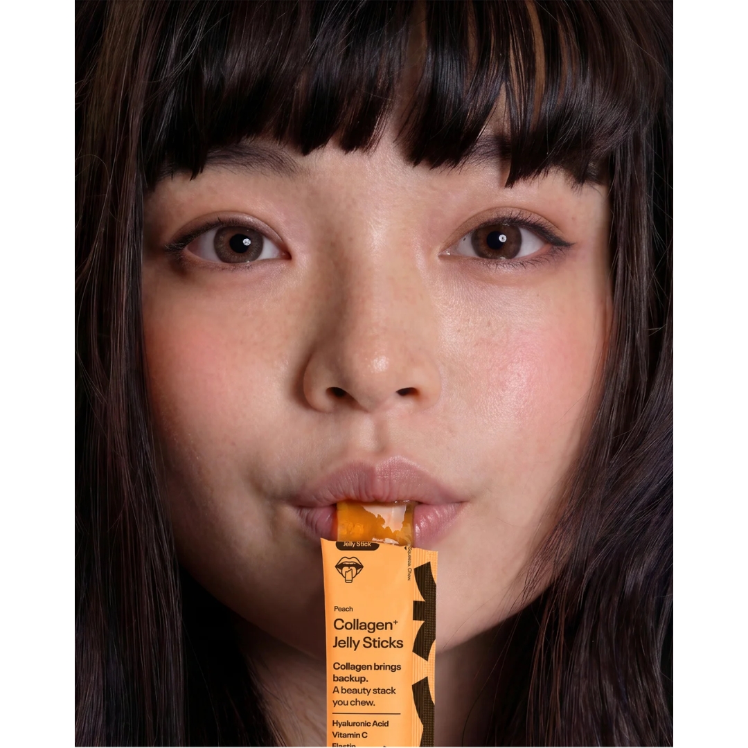 A model holds a Rin Collagen+ Jelly Stick in Peach to her lips, with the jelly poking out of the sachet.