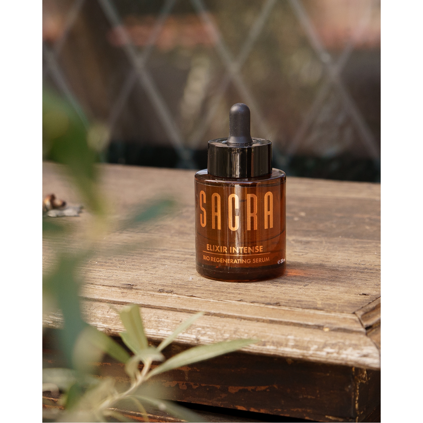 An amber glass bottle of Sacra Elixir Intense Bio Regenerating Serum sitting on a rustic wooden table, featured in the brand's UK launch announcement on Beauty News Daily.