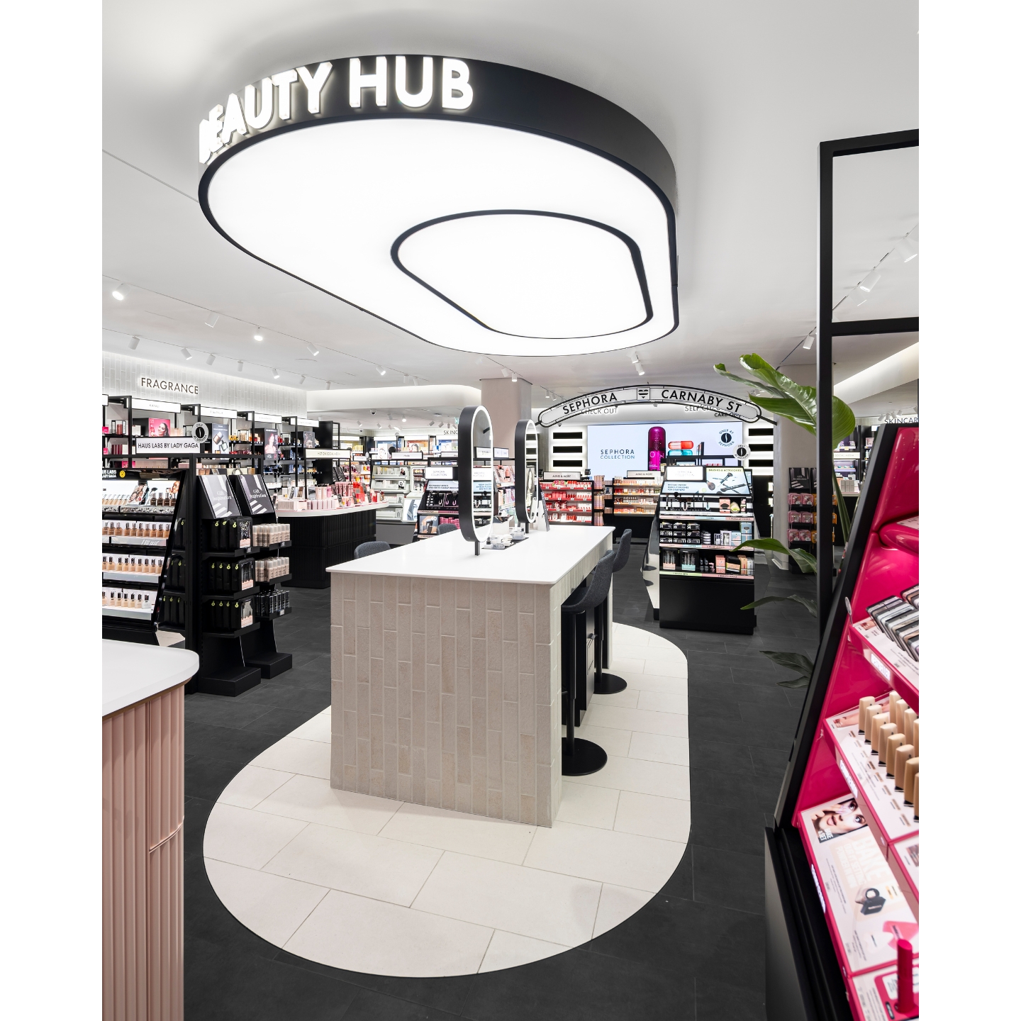 Interior view of the Sephora UK Carnaby Street store in London featuring a central 'Beauty Hub' testing counter with lighted mirrors, surrounded by brand displays and a 'Sephora Carnaby St' sign above the checkout.