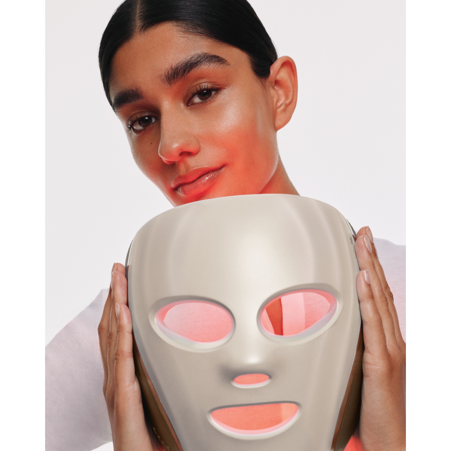 Model holding a silver Shark Beauty CryoGlow LED face mask with red light therapy glowing through the eye and mouth openings.