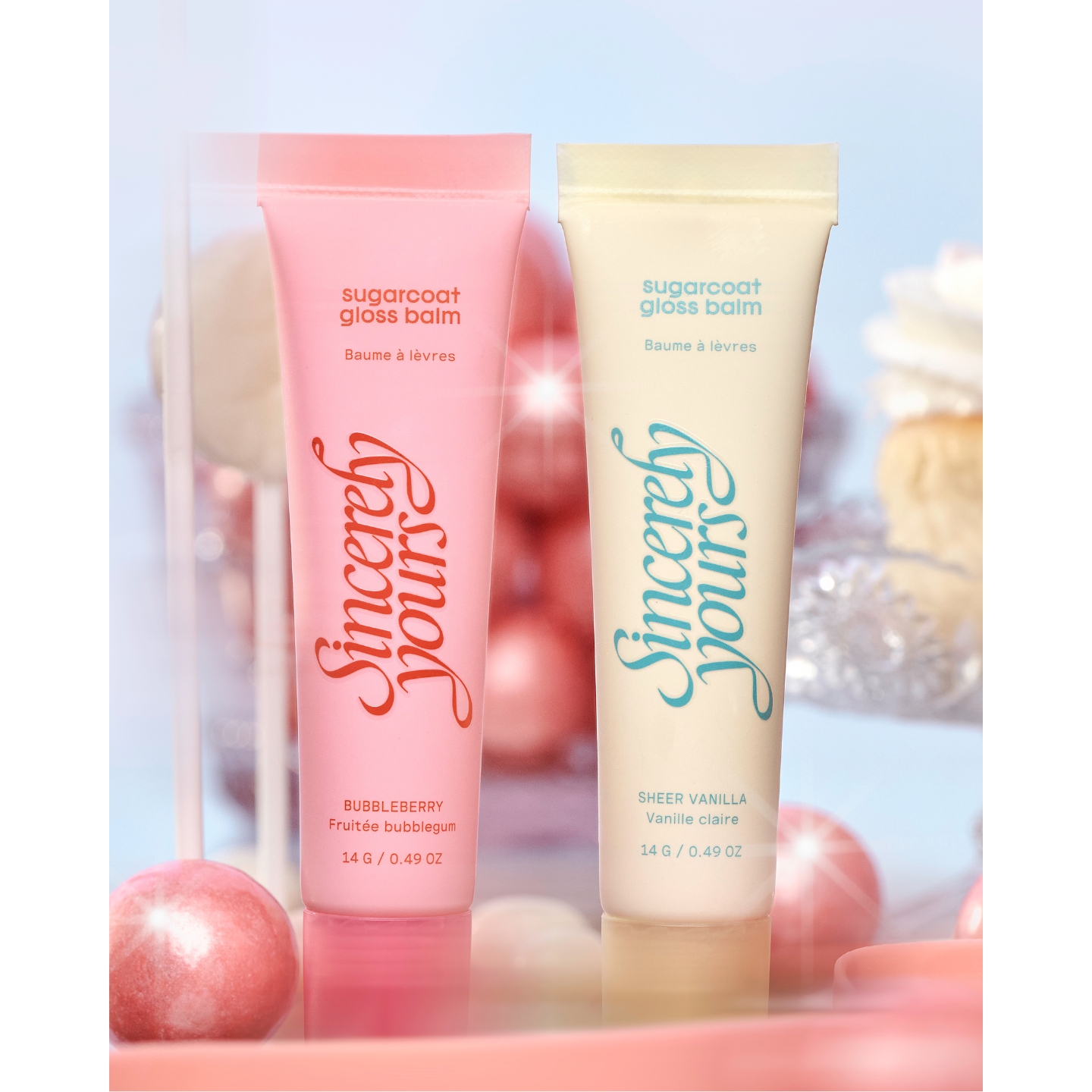 Two tubes of Sincerely Yours Sugarcoat Gloss Balm in Bubbleberry and Sheer Vanilla against a soft pink candy backdrop, featured in the Jordan Salish interview on Beauty News Daily.