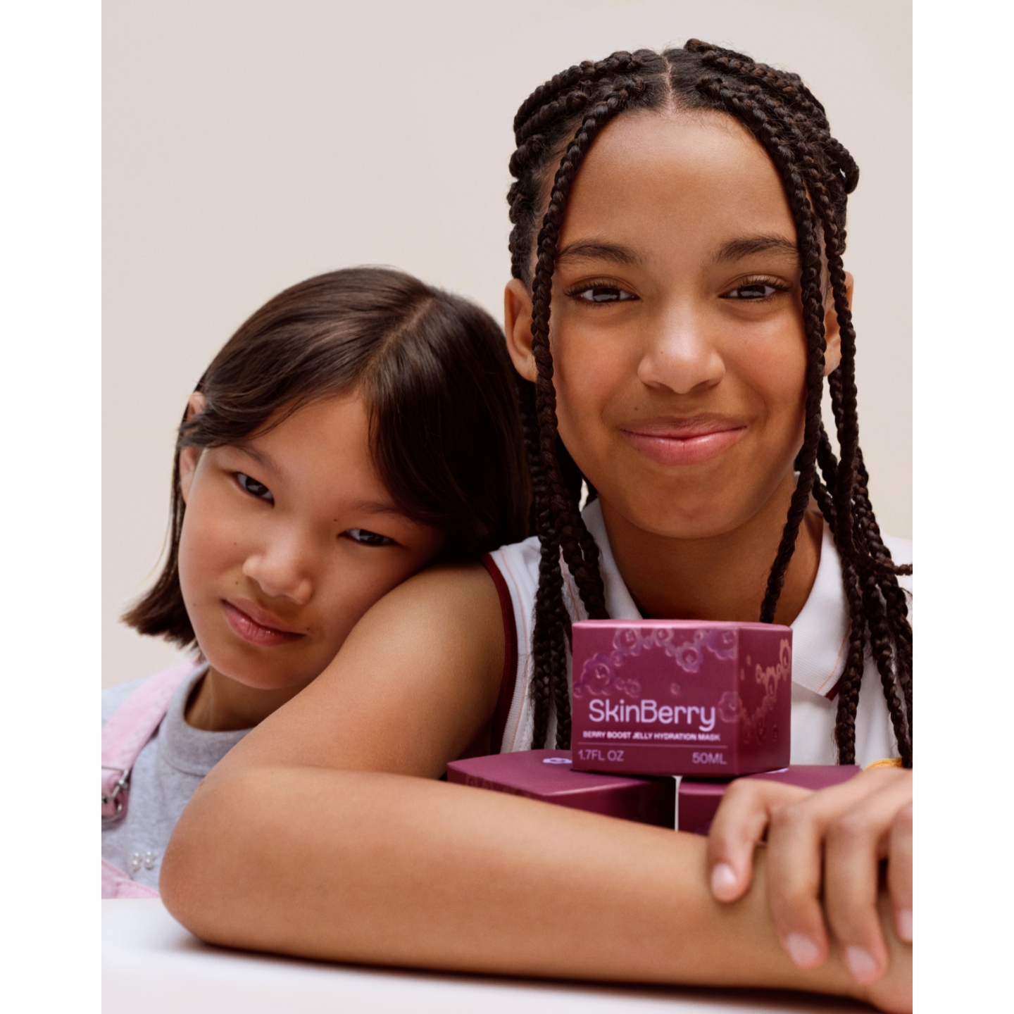 Two young models posing together behind stacked plum boxes of SkinBerry Berry Boost Jelly Hydration Mask on a light beige background.