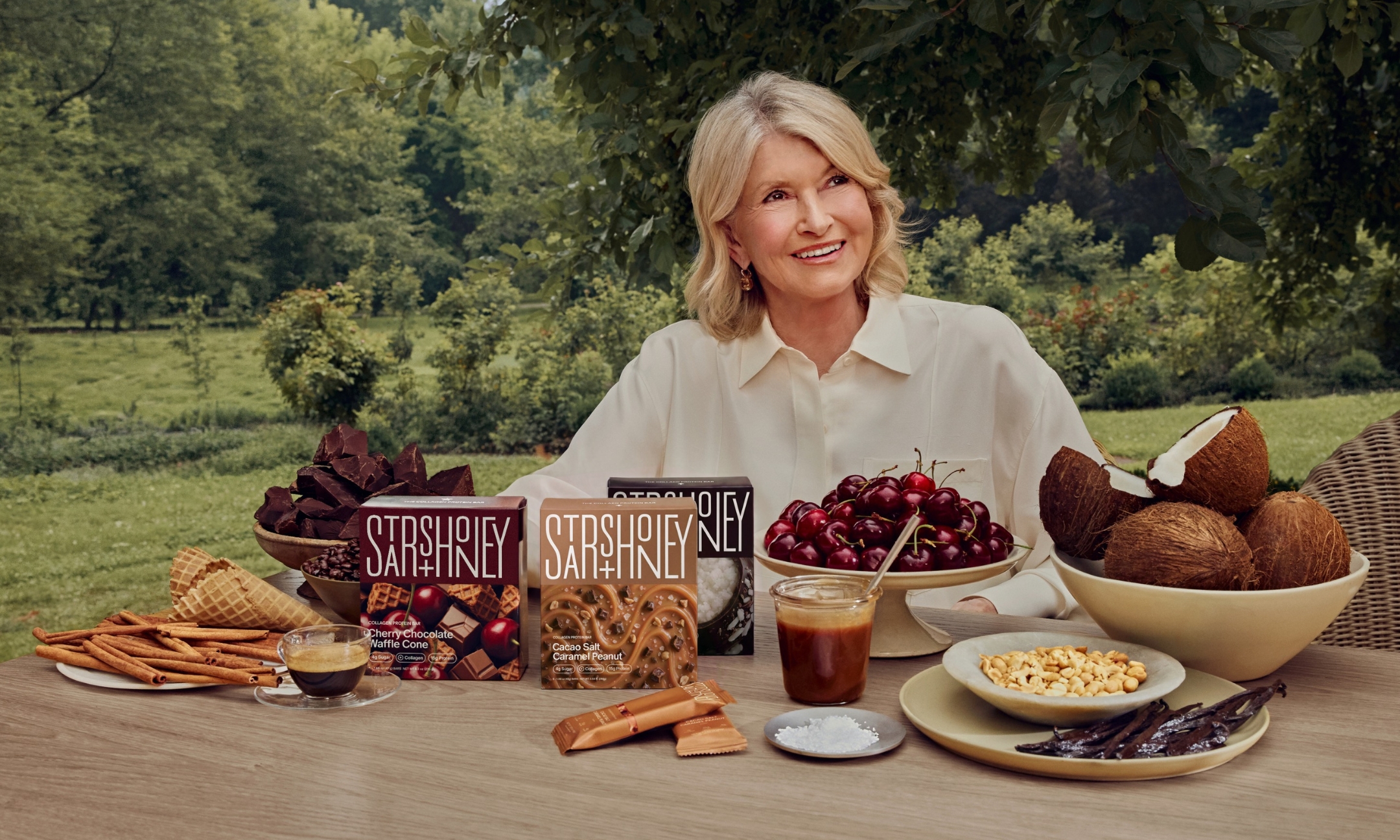 Martha Stewart at a garden table with Stars + Honey collagen protein bars and fresh ingredients including cherries and coconuts.