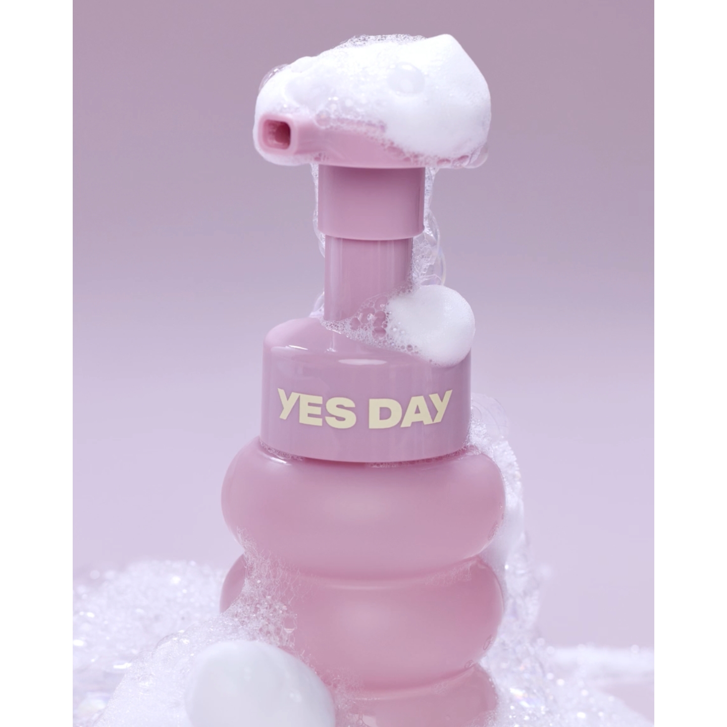 A close-up of the pastel purple pump bottle of Yes Day Float Foam Face Cleanser covered in white soapy bubbles, featured on Beauty News Daily.