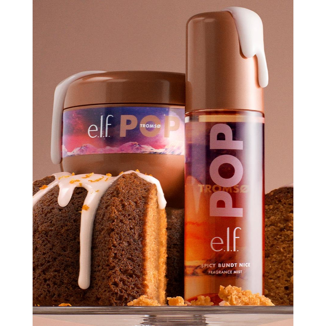 A bottle of e.l.f. Pop Tromsø Spicy Bundt Nice Fragrance Mist and matching body cream tub styled with white icing dripping down the containers beside sliced spiced bundt cake.