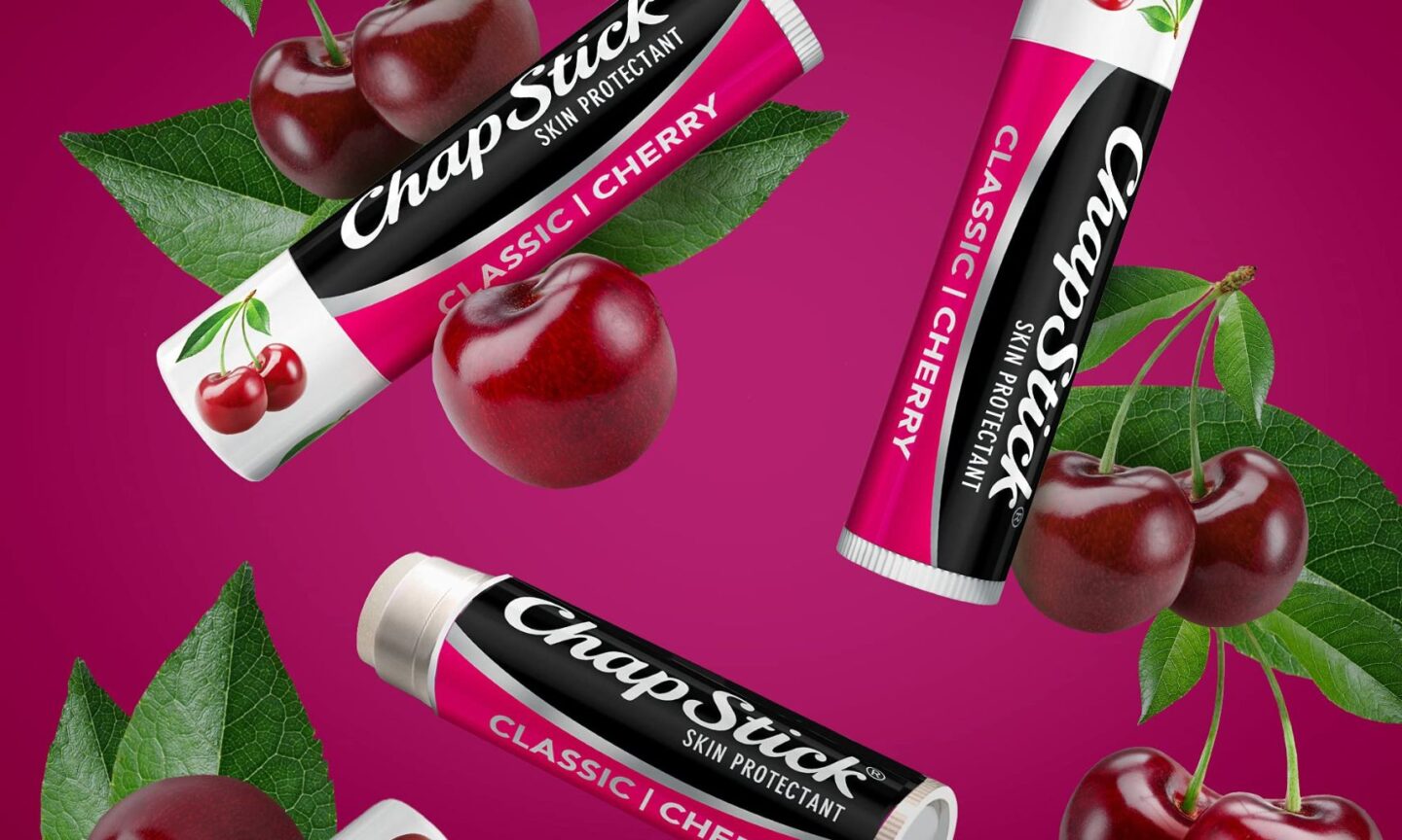 three Cherry ChapSticks on a purple background surrounded by cherries